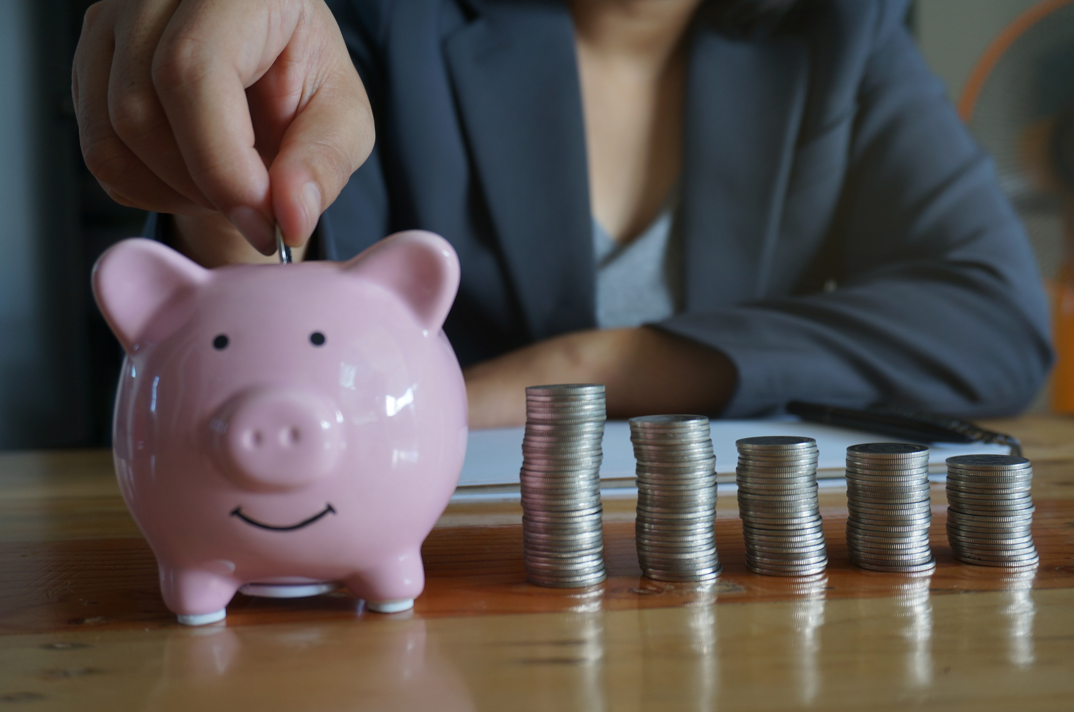 Professional woman with coins placing money in a piggy bank
